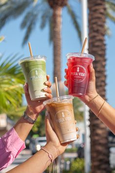 three people holding up drinks in front of palm trees