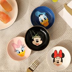 three mickey mouse plates with cartoon faces on them next to silverware and utensils