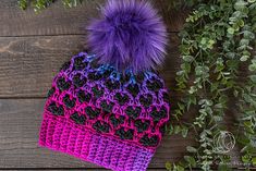 a crocheted hat with a purple and black pom - pom