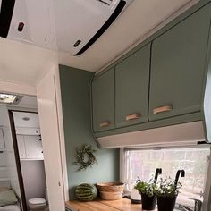 an rv kitchen with green cabinets and wood counter tops, along with potted plants