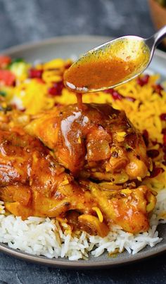 a spoon is being used to stir chicken over rice on a plate with other food