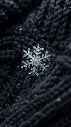 a snowflake is sitting on the black knitted material that looks like it has been made out of yarn