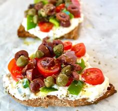 two pieces of bread with tomatoes, olives and other toppings on top of them