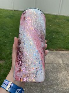 a person holding up a pink and blue glittered drink in front of a white building