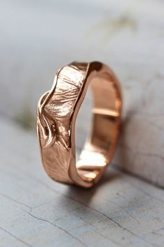 a rose gold wedding ring on top of a piece of white wood with a leaf design