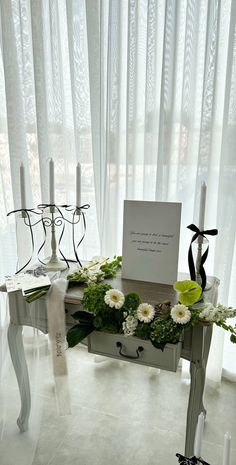 a table with flowers and candles on it in front of a window covered by sheer curtains