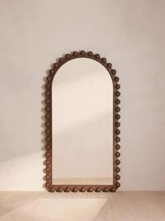 a mirror sitting on top of a wooden floor next to a white wall with a brown frame