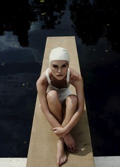 a woman sitting on the edge of a dock wearing a bathing suit and headband