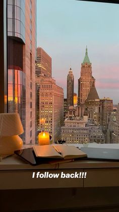 an open book sitting on top of a window sill in front of a city skyline