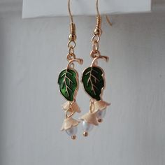 Of The Earth Gold and Green Floral Pearl Earrings A delicate painted evergreen leaf hangs from pearlescent beaded metal flowers, putting an eclectic and unusual spin on the classic, timeless imagery of fresh budding spring. Lightweight and lovely, for day or night. A corresponding choker, additional pair of earrings, a body chain and a ring make up this collection. Everyday wear made interesting; a simple, elegant design for any nature lover.  Carefully crafted and lovingly handmade on the Scott Nature-inspired Dangle Earrings With Flower Charm, Nature-inspired Flower Earrings, Nature-inspired Dangle Flower Earrings, Green Flower-shaped Nature-inspired Earrings, Nature-inspired Green Flower Earrings, Nature-inspired Flower Charm Drop Earrings, Nature-inspired Green Dangle Flower Earrings, Nature-inspired Birth Flower Earrings, One Of One