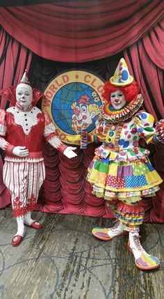 two clowns standing on stage in front of a red curtain