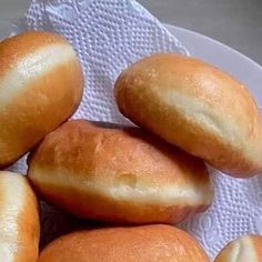 a white plate topped with bread rolls on top of a cloth covered table next to a knife