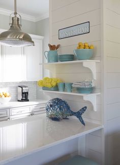 a white kitchen with blue and yellow dishes on the shelves, under a hanging light