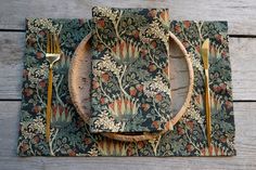 a place setting on a wooden table with floral napkins and gold cutlery,