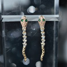 A ladies pair of 14 karat yellow gold snake dangle earrings set with 54 round brilliant cut diamonds having a total weight of .29 carats and 4 round emerald eyes having a total weight of .03 carats. Formal 14k Gold Earrings With Diamond Eyes, Luxury White Gold Earrings With Diamond Eyes, Handmade Gold Snake-shaped Earrings, Luxury Gold Earrings With Diamond Eyes, Gold Earrings With Cubic Zirconia Diamond Eyes, Gold Drop Earrings With Diamond Eyes, Yellow Gold Earrings With Diamond Eyes For Wedding, Handmade Gold Cubic Zirconia Earrings, Gold Snake Shape Single Earring