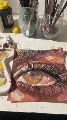 an eye is shown on the table next to some paint brushes and other art supplies