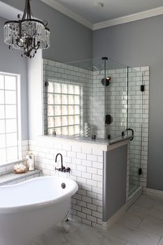 a white tub sitting next to a shower in a bathroom under a chandelier