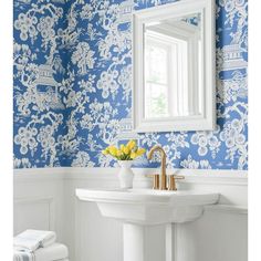 a bathroom with blue and white wallpaper, gold faucet, sink and mirror