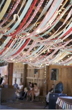 many ribbons are hanging from the ceiling in a room with people sitting and standing around