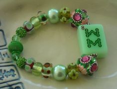 "This mint green Mahjong bracelet is made with an \"8 Bam\" Mahjong tile in the center. The tile is a light green color. The beads are shades of green with touches of pink Jesse James beads. Jesse James beads are very unusual. I use them a lot because they are unique and high quality. This bracelet is made on stretch cord and fits up to an 8 inch wrist. The stretch cord makes this jewelry easy to get on and off.  This bracelet is a perfect Mahjong gift for yourself or any of your Mahjong playing friends. It comes in a decorative gift box for easy gifting. Buy several for your Mahjong friends. I am offering free shipping in the U.S." Rectangular Green Bracelets As Gifts, Green Rectangular Bracelets As Gifts, Adjustable Green Bracelets With Letter Beads, Green Personalized Bracelets With Round Beads, Personalized Green Bracelets With Round Beads, Personalized Green Bracelets For Friendship, Personalized Green Jewelry For Friendship, Casual Green Stretch Bracelet With Letter Beads, Personalized Green Beaded Bracelets For Friendship