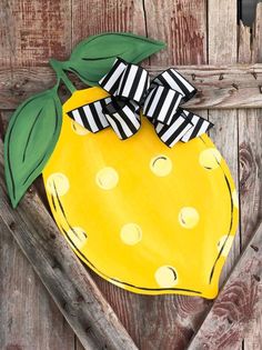 a painted yellow and black apple with a bow on it's head is hanging on a wooden fence