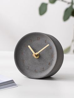 a grey clock sitting on top of a table next to a vase filled with flowers