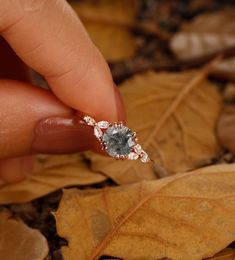 a person's hand holding an engagement ring with a blue diamond in it on top of leaves