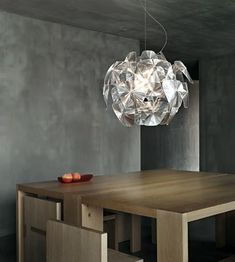 a modern light fixture hanging over a wooden table in a room with grey walls and chairs