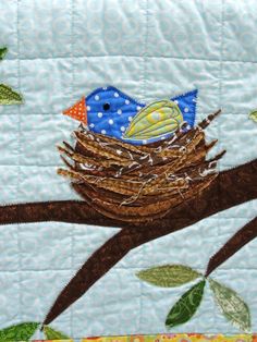 a blue bird sitting on top of a tree branch next to a green leaf filled wall hanging