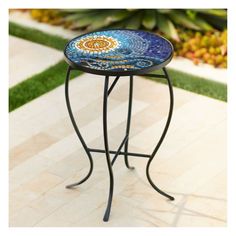 a small table with a blue and yellow mosaic design on it's top sitting in the middle of a garden