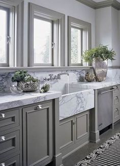 a large kitchen with marble counter tops and gray cabinetry, along with two sinks