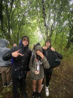 three people standing in the woods with one pointing at something while the other holds up his finger