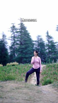 a woman standing in the grass talking on her cell phone with trees in the background