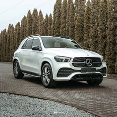 a white mercedes benz suv parked in front of some bushes and trees on a brick road