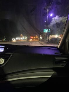 the dashboard of a car at night with street lights in the back ground and cars driving down the road