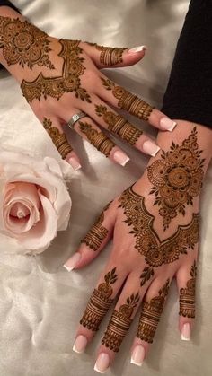 two hands with henna tattoos on them and a rose in the middle, one hand is