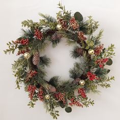 a christmas wreath with pine cones, berries and evergreens on white wall background ornament