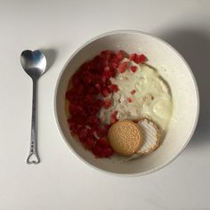 a white bowl filled with food next to a cookie and spoon on top of a table