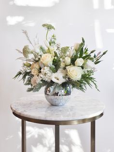 a vase filled with white flowers sitting on top of a marble topped table next to a wall