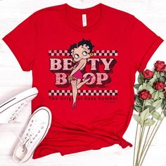 "Betty Boop T-shirt, Original Sass Tee, Officially Licensed Betty Boop Merchandise Shirt, Checkered, Symbol, American Icon, Red Dress * Fashion fit * Clothing style: Athletic * Neckline: Crewneck * Sleeve length: Short sleeve Handmade in our shop with high quality retail printing on a high quality Bella + Canvas fashion t-shirt. Solid Colors - 4.2 oz.(US) 7 oz.(CA), 100% Airlume combed and ringspun cotton Heather Colors - 4.2 oz.(US) 7 oz.(CA), 52/48 Airlume combed and ringspun cotton/polyester Red Cartoon Print Graphic Tee, Red Graphic Tee With Cartoon Print, Red Crew Neck Shirt With Cartoon Print, Red Graphic Tee With Funny Print, Pop Culture Red Top With Character Print, Red Pop Culture Top With Character Print, Red Crew Neck Top With Funny Print, Trendy Red T-shirt With Character Print, Red Cotton T-shirt With Cartoon Print