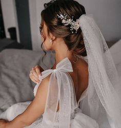 a woman sitting on top of a bed wearing a white dress and veil with flowers in her hair