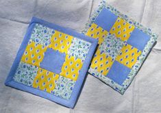 two square quilts are sitting next to each other on a white sheet with blue and yellow designs