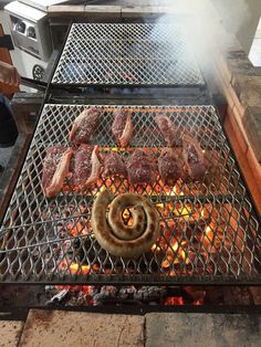 an outdoor grill with meat and buns cooking on it's burners,