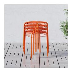 an orange metal stool sitting on top of a tiled floor next to a potted plant