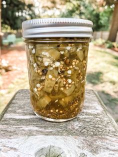 a jar filled with pickles sitting on top of a cement slab in the grass