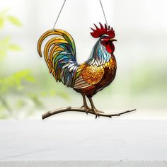 a stained glass rooster sitting on a branch with chains hanging from it's neck