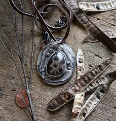 "Sterling Silver, Copper, Petoskey stone all in one.  Beautiful stone on the handmade necklace with hand stamped silver and a copper back speaking the same language as the stone.  All on a leather cord of 36\" with trade bead types on the ends.  You could say this represents the stars, the sun  (pattern on the stone) and the water, as that is where the stones are generally found.  This very organic necklace is approximately 1-3/4\" wide and 2\" long.  Shipping to United States only." Artisan Stamped Brown Jewelry, Rustic Leather Stamped Jewelry, Artisan Hand Tooled Jewelry, Unique Brown Stamped Jewelry, Hand-tooled Silver Leather Jewelry, Rustic Hand-tooled Silver Jewelry, Bead Types, Organic Necklace, Sun Pattern