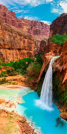 a waterfall in the middle of a canyon with blue water and green plants on either side