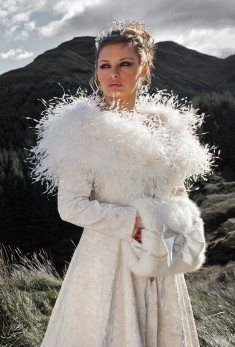 a woman in a white dress and fur stoler standing on top of a hill