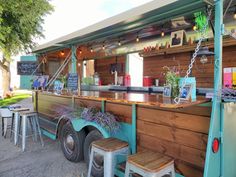 an outdoor food truck with plants on the outside bar and stools at the front